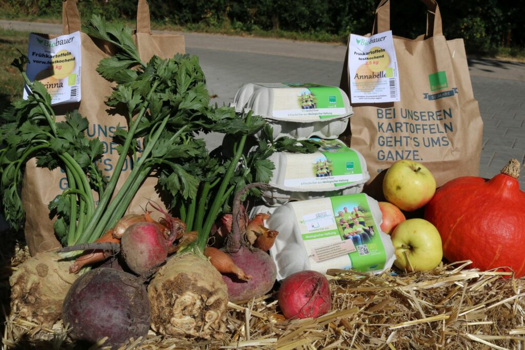 Auf Heuballen sind Eierschachteln und verschiedene Gemüse- und Obstsorten aufgestellt.