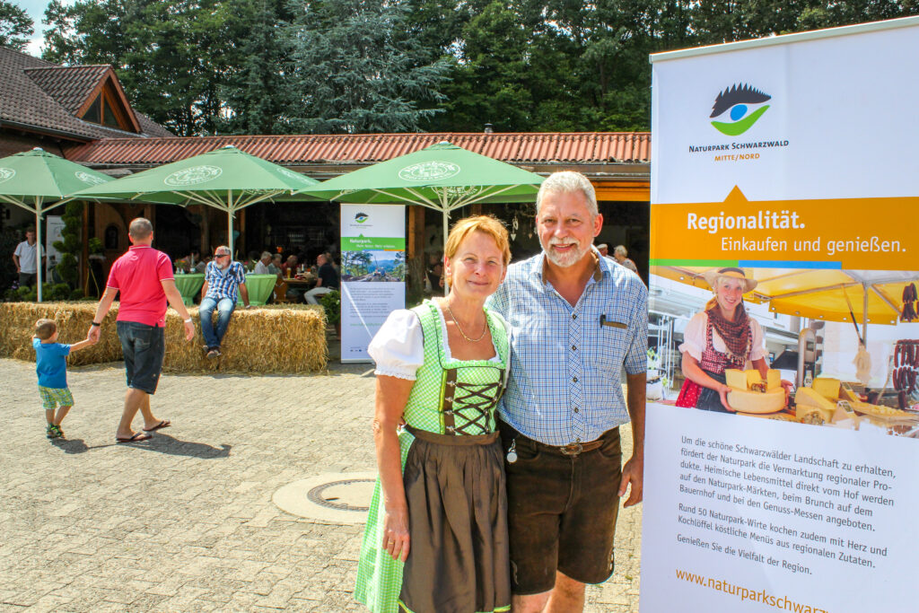 Ein Mann und eine Frau stehen vor dem Info-Roll-up zum Naturpark-Brunch auf dem Bauernhof.