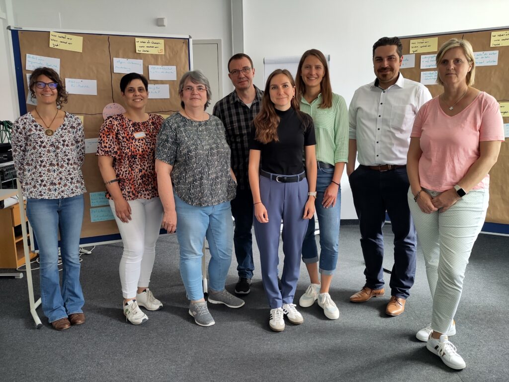 acht Männer und Frauen stehen nebeneinander in einem Raum