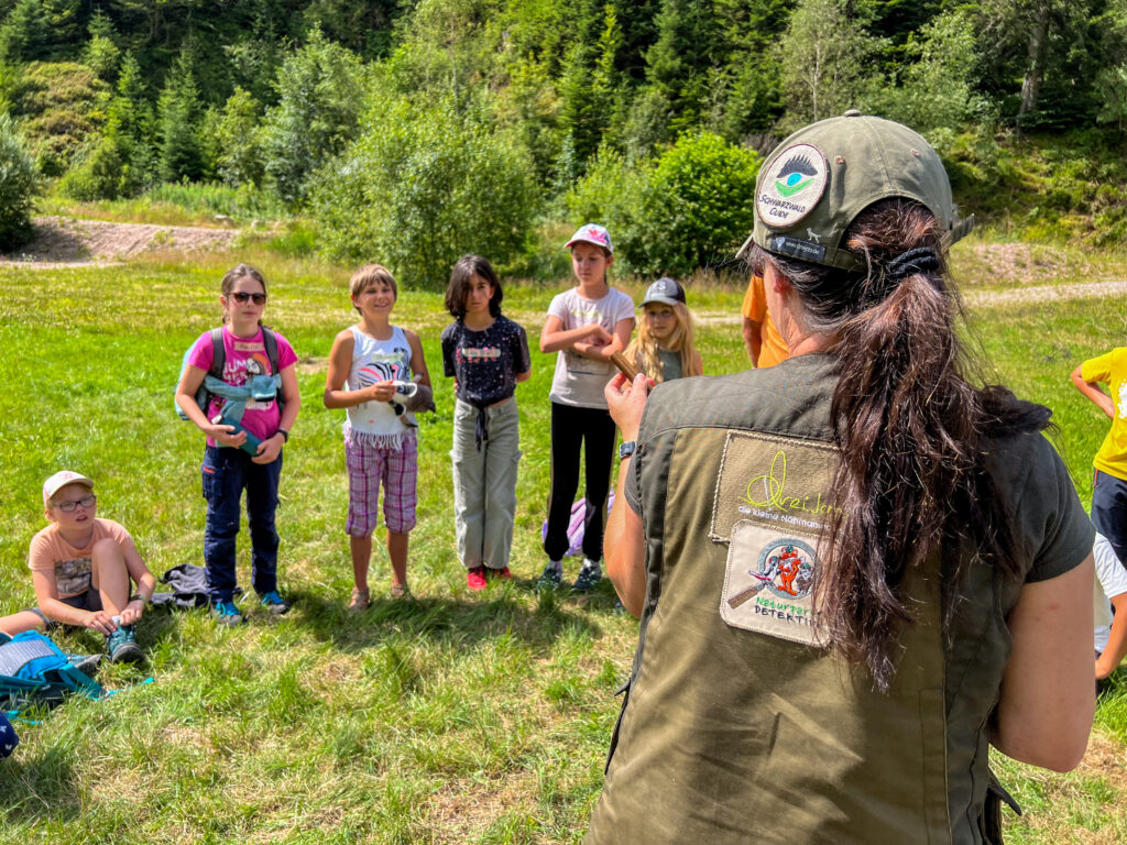 Eine Frau erklärt Schülern auf einer Wiese etwas