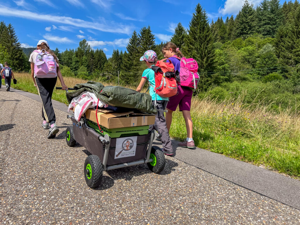 Kinder ziehen einen beladenen Bollerwagen