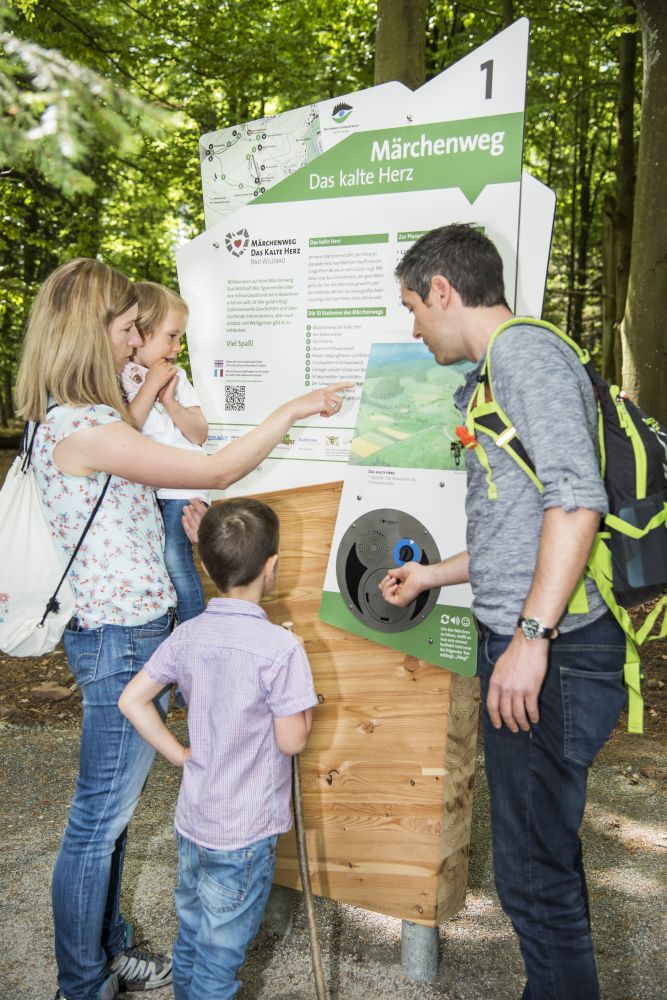 Eine Familie steht vor einer interaktiven Infotafel.