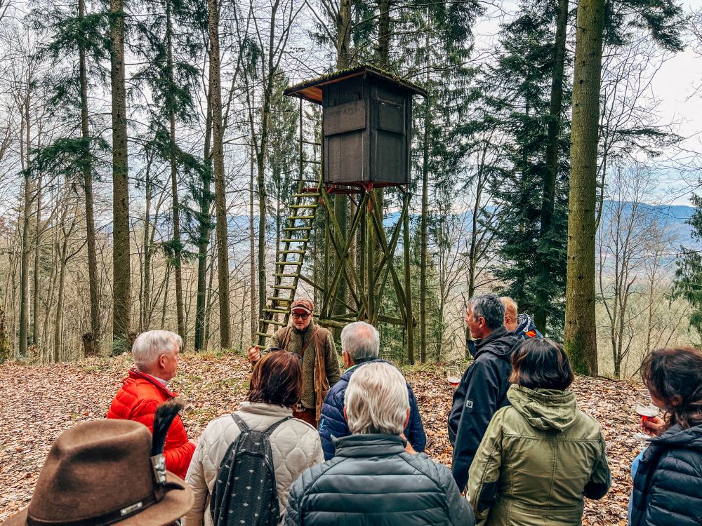Jäger erklärt einer Gruppe von Menschen etwas auf einem Pirschgang vor einem Hochsitz im Wald.