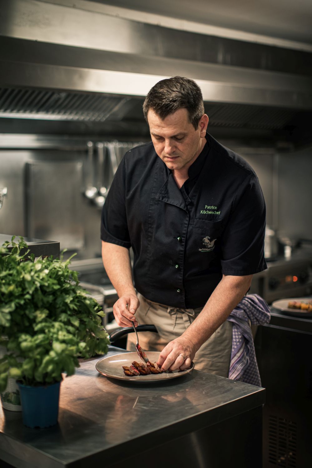 Koch richtet Wilde Sau-Gericht auf einem Teller in der Küche an.