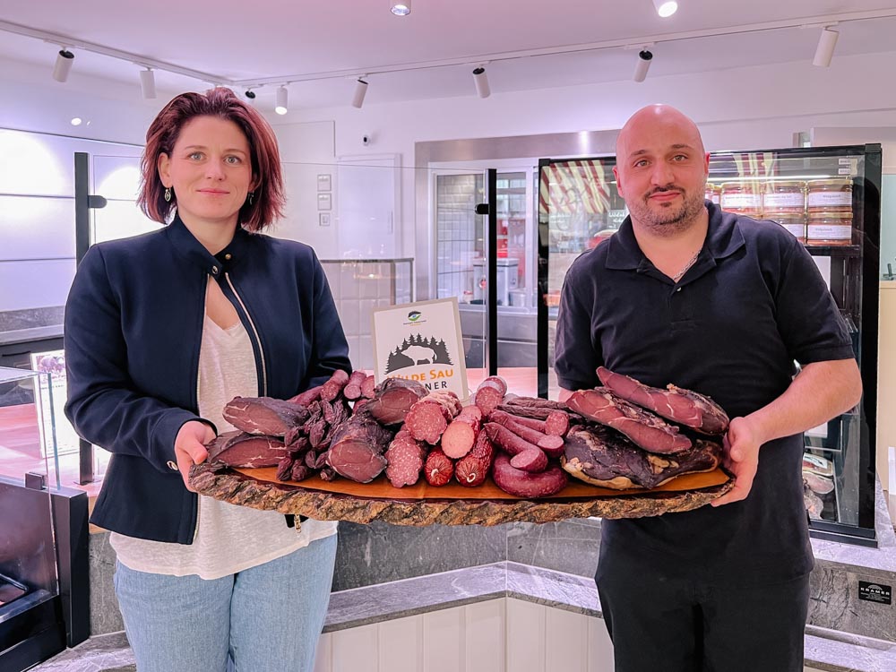 Judith Wohlfahrt und Alexander Ehret halten ein großes Holzbrett mit Wilde Sau-Spezialitäten und der Wilde Sau-Partnerplakette in den Händen.