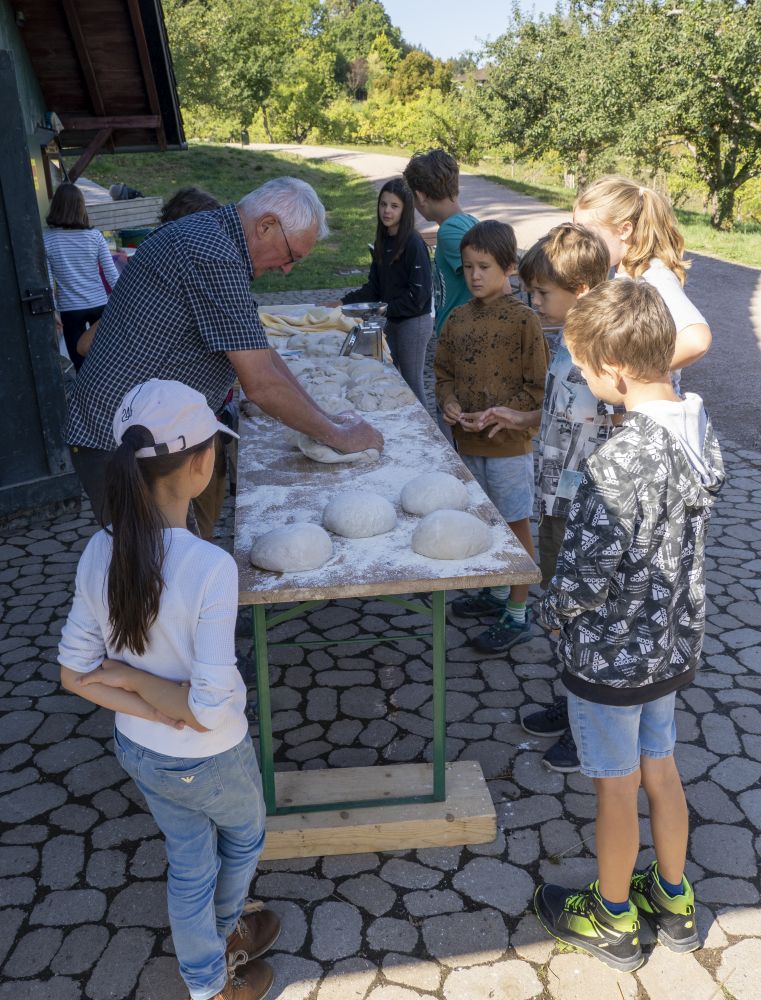 Ein Mann knetet Brotlaibe, Kinder schauen zu.