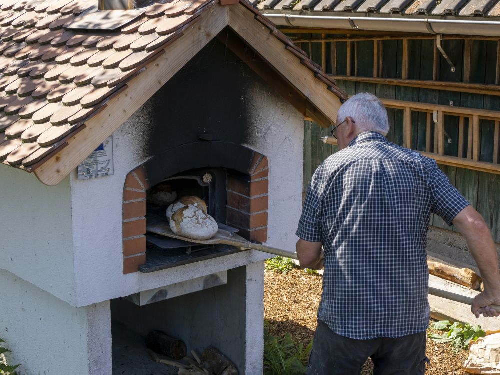 Ein Mann holt einen Brotlaib aus einem Holzbackofen im Freien.