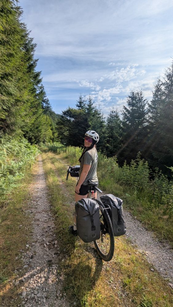 Frau mit ihrem Gravel Bike und Trekking-Gepäck auf einem Forstweg im Wald
