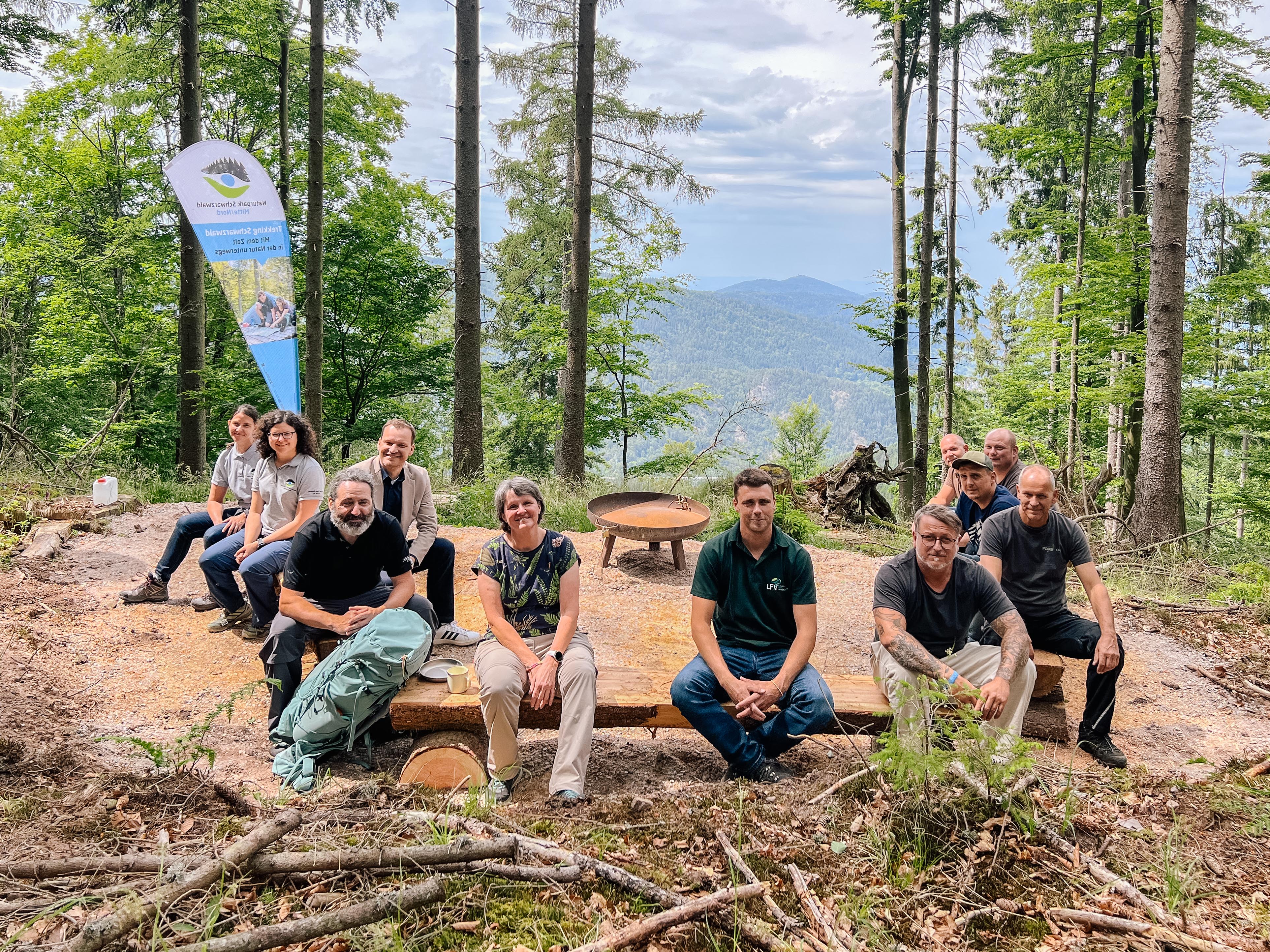 Menschen sitzen bei der Eröffnung des Camps auf Baumstammbänken um  die Feuerschale herum