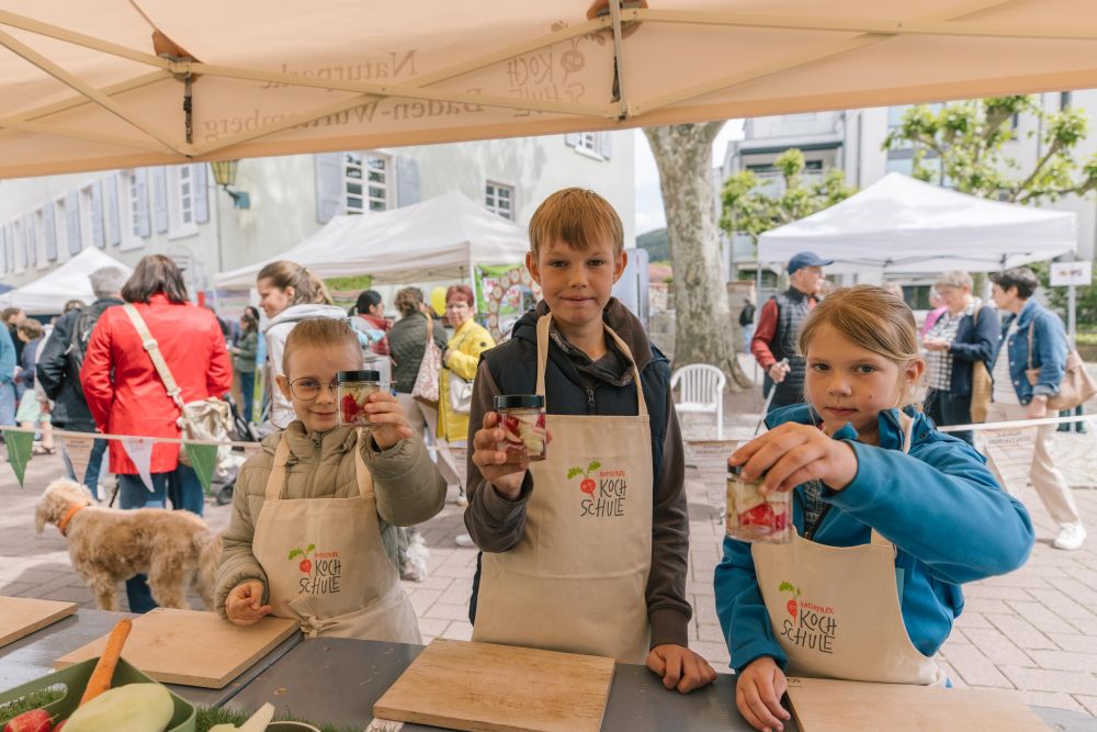 Drei Kinder zeigen ihr selbstgemachtes Eingemachtes in Gläsern.