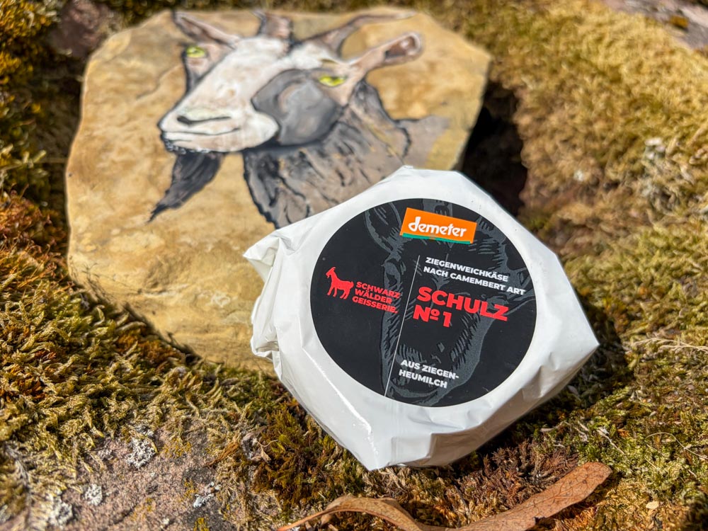 verpackter Camembert liegt auf einem Stein mit einem Ziegenbild