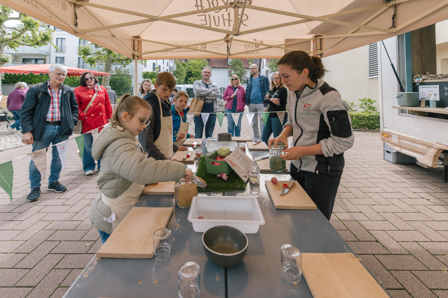 Kinder schneiden Gemüse unter fachlicher Anleitung an einem Marktstand.