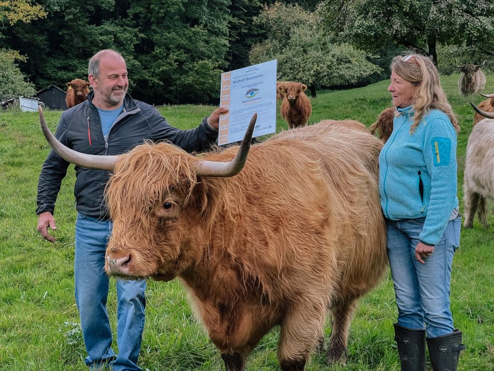 Die Baumanns mit der Partner-Plakette und einem Hochlandrind auf der Weide