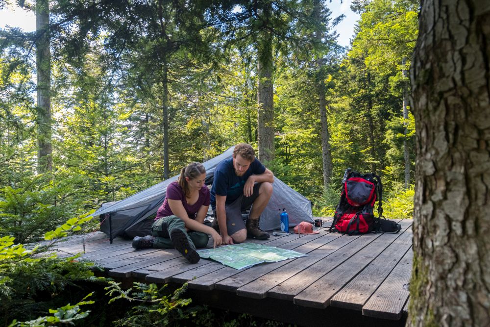 Ein Mann und eine Frau schauen sich vor ihrem Zelt eine Wanderkarte an.