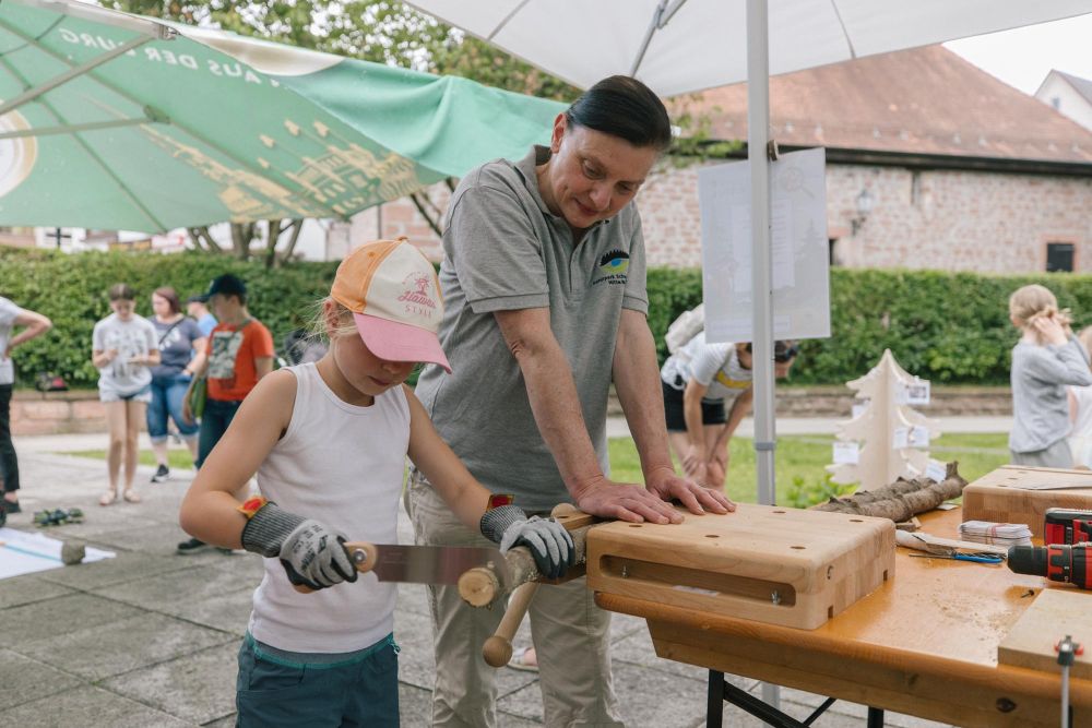 Naturpark-Mitarbeiterin sägt mit Kind ein Holzstück.