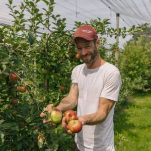 Landwirt Johannes Lorenz steht zwischen seinen Apfelbäumen und hält Äpfel in der Hand.