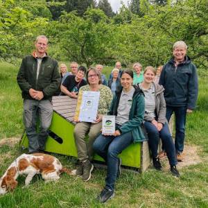 Menschen sitzen auf einer Holzliege inmitten einer Streuobstwiese