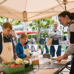 Eine Frau schneidet mit Kindern an einem Tisch Gemüse.