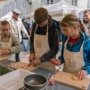 Drei Kinder schnippeln Gemüse in einer Küche auf einem Markt.