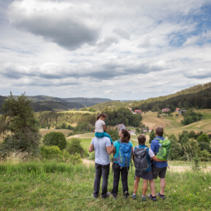 Eine Familie steht auf einer Wiese und schaut auf die Kulturlandschaft mit Wiesen, Weiden, Wäldern und Höfen.