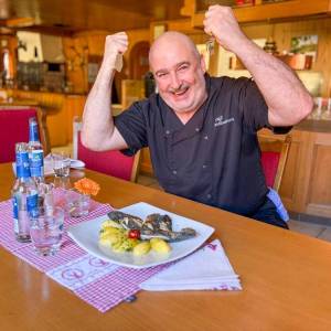 Küchenchef Ralf Finkbeiner hält Gabel und Fischmesser in den Händen, sitzt am gedeckten Tisch mit seiner frisch zubereiteten Schwarzwaldforelle 