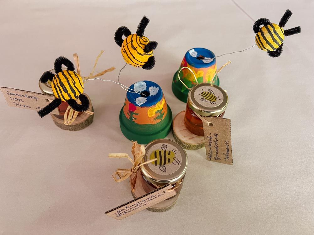 gebastelte Bienen fliegen über bemalten kleinen Blumentöpfen, kleine Honiggläser