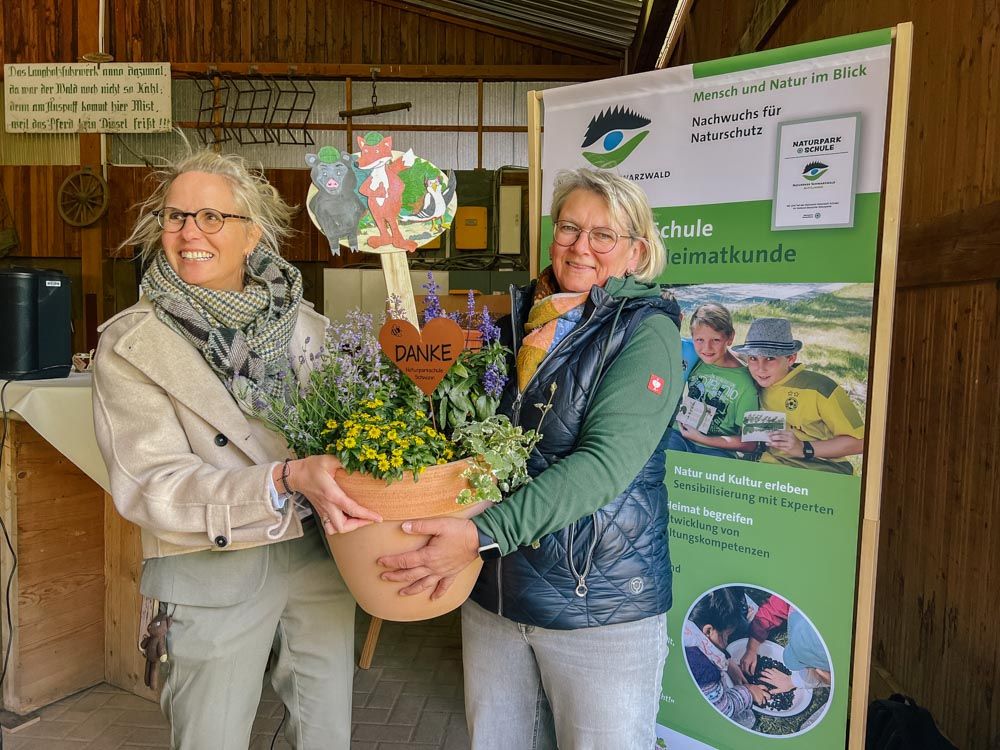Schulleiterin Elisabeth Kiebelstein überreicht Elke Reiser vom Biolandhof Reiser einen bepflanzten Kübel mit einem Naturpark-Detektive-Schild.