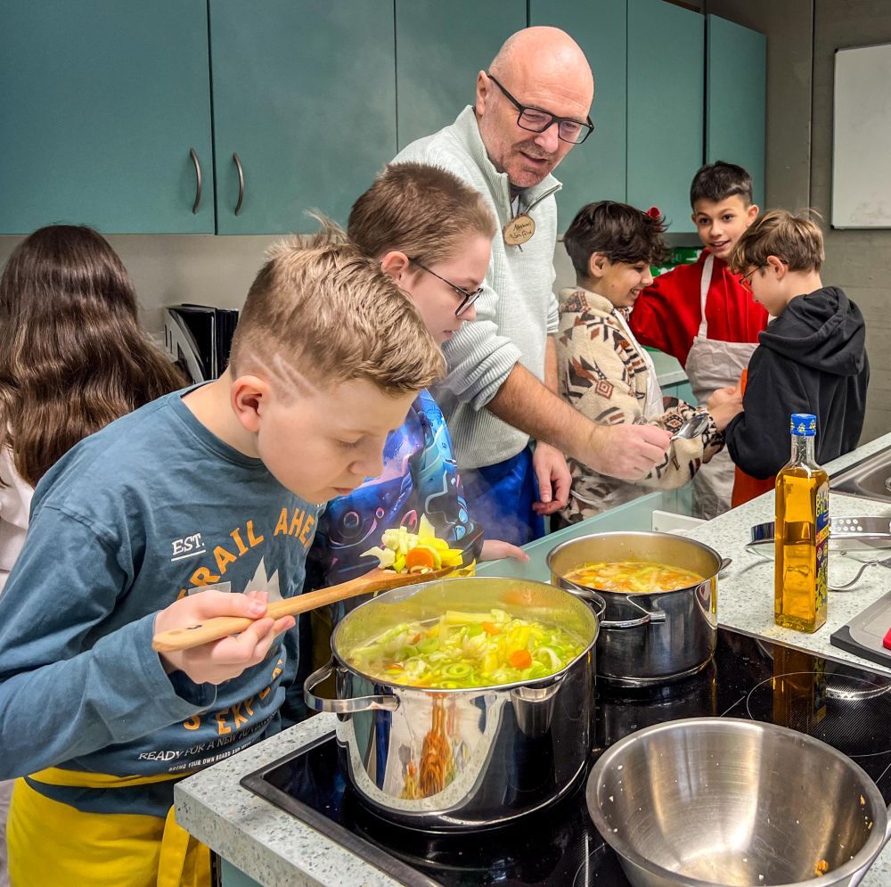 Ein Mann kocht mit Kindern einen Gemüseeintopf.