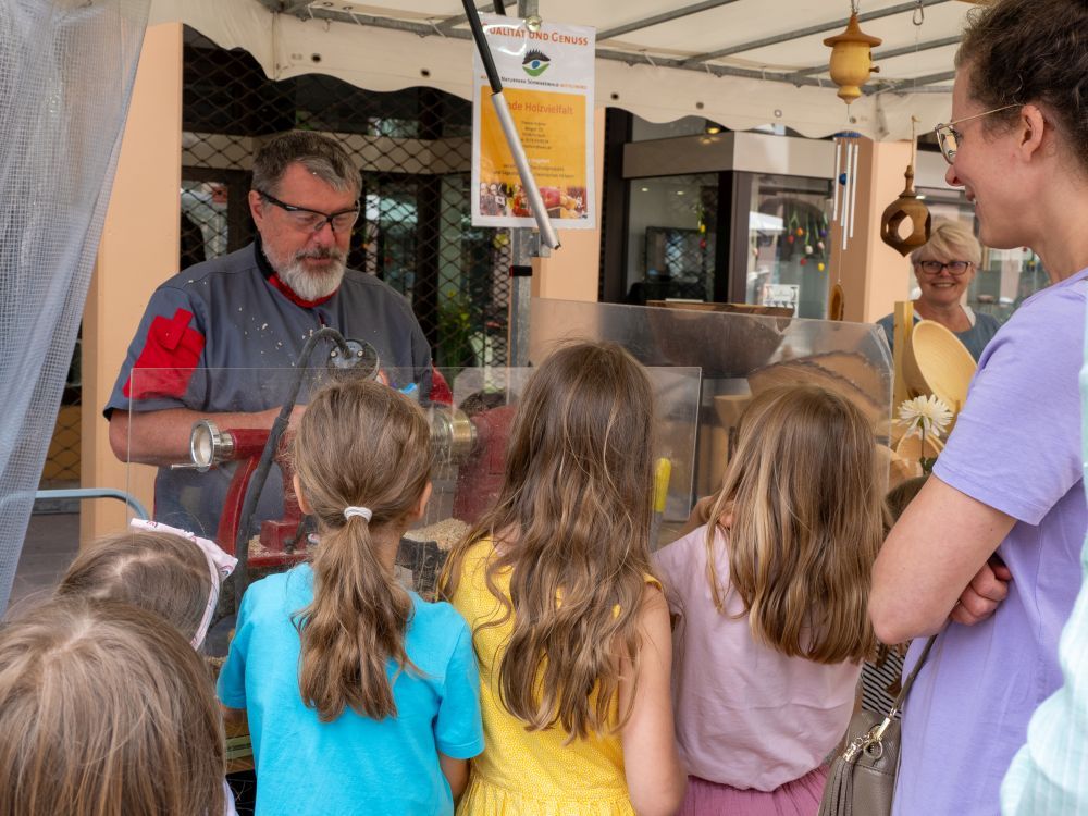Kinder schauen einem Dechsler an der Werkbank zu.