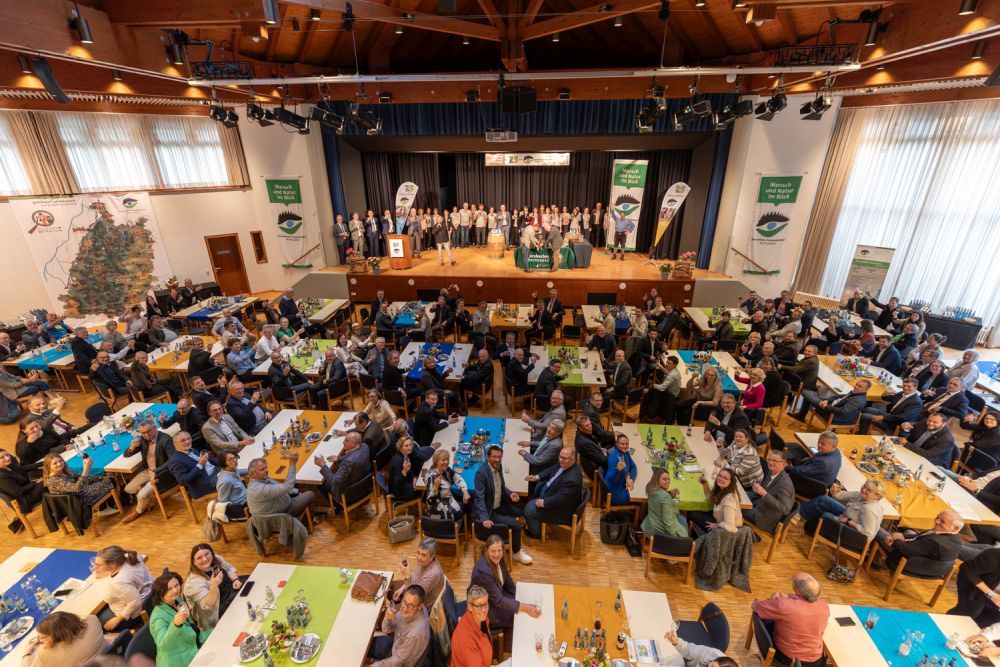 Menschen sitzen in einem großen Saal und prosten dem Fotografen zu.