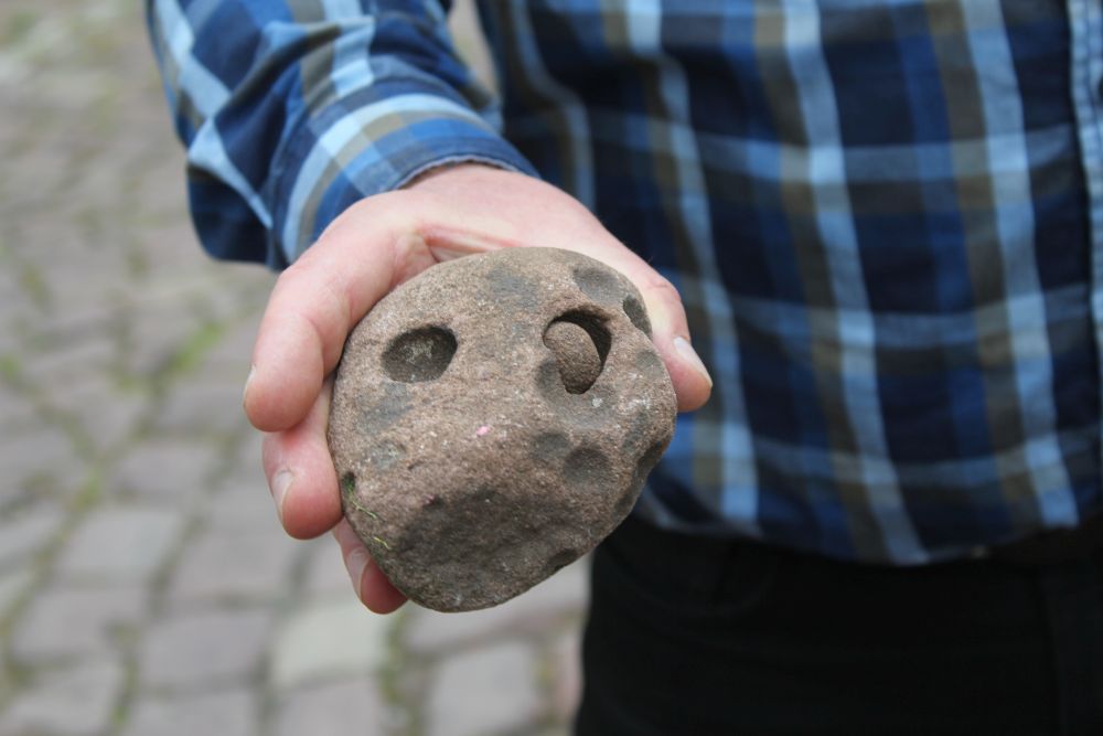 In einem größeren Stein sind zwei Kuhlen. In einer liegt ein kleiner, runder Stein.