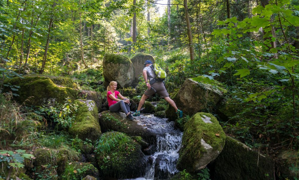 Mann springt über einen Bach im Wald.