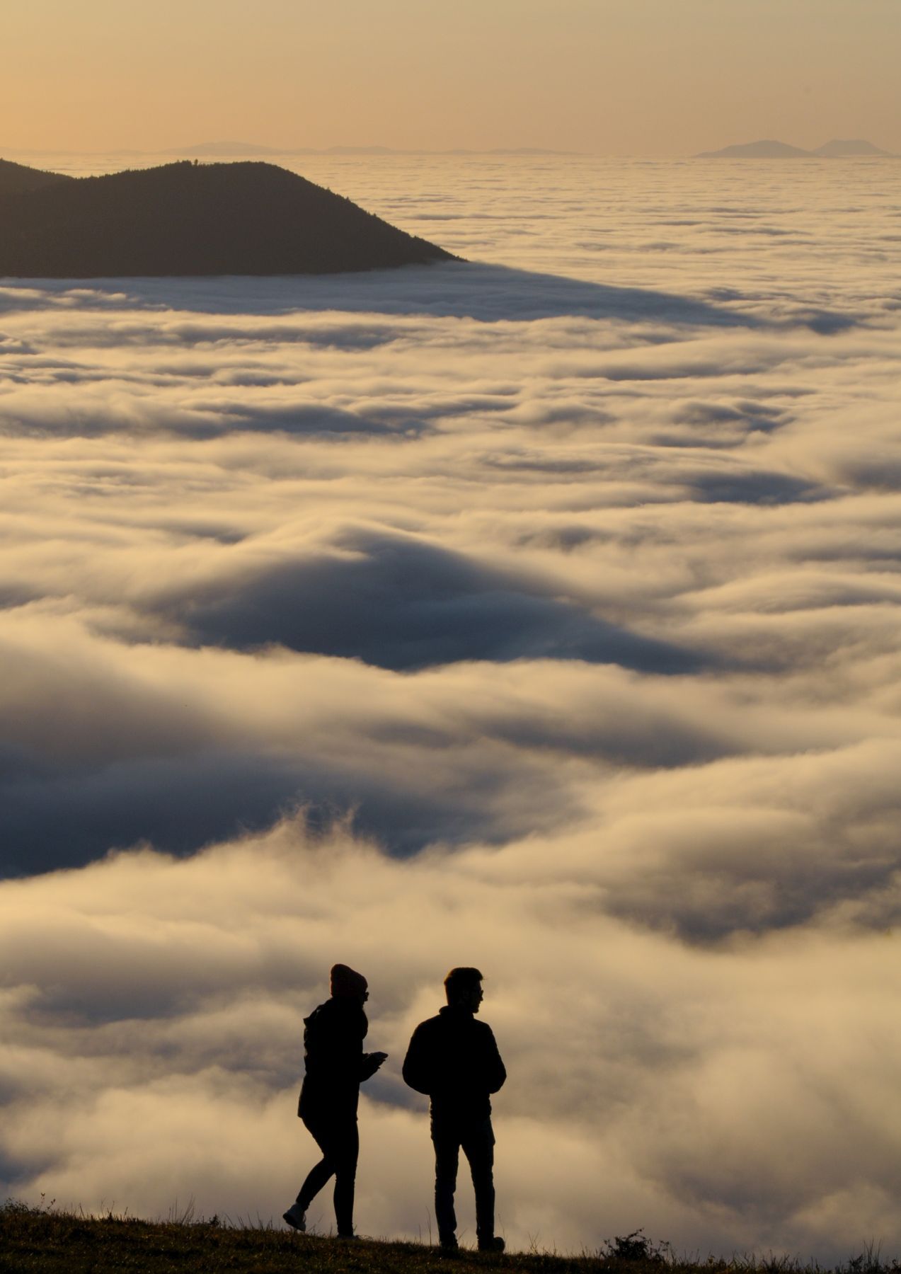 Zwei Menschen stehen auf einem Hügel und schauen auf ein Wolkenmeer. Foto: Albert Koch