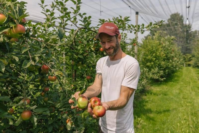 Landwirt Johannes Lorenz steht zwischen seinen Apfelbäumen und hält Äpfel in der Hand.