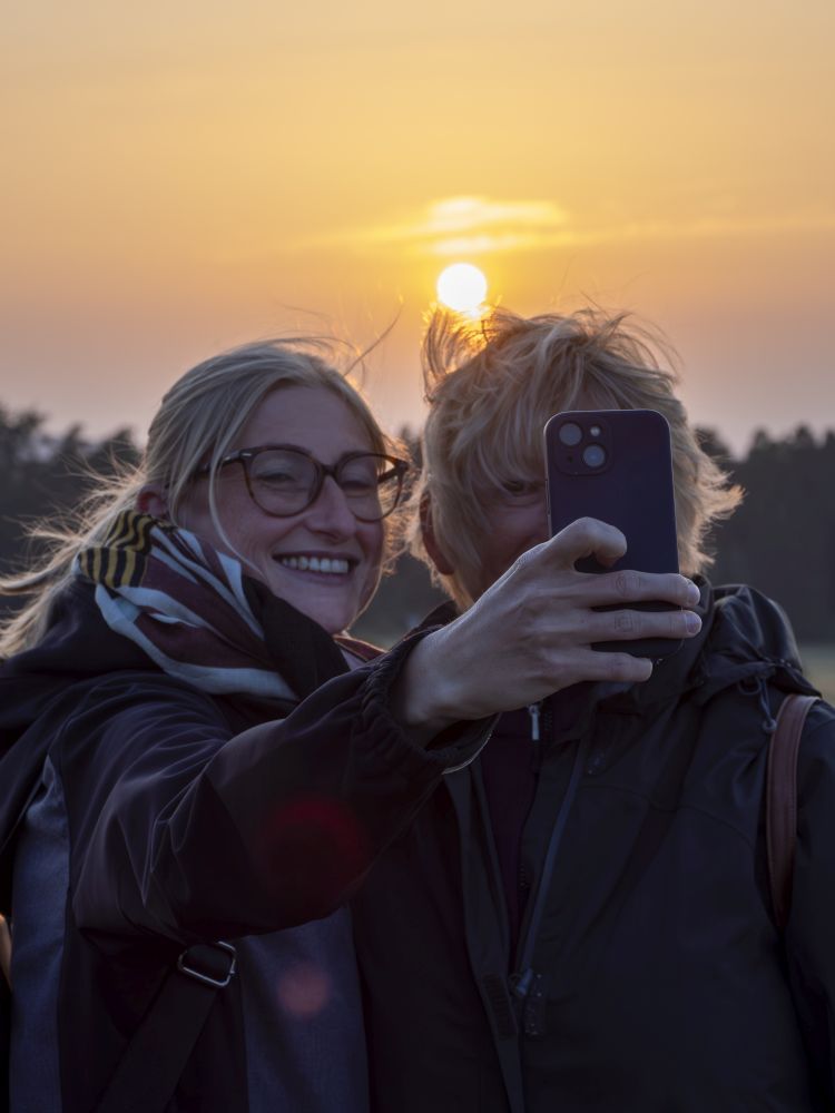Zwei Frauen machen vor der untergehenden Sonne ein Selfie.