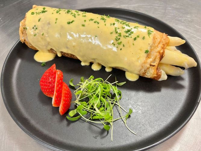 Spargel in einem Pfannkuchen eingehüllt mit Sauce Hollandaise auf einem schwarzen Teller