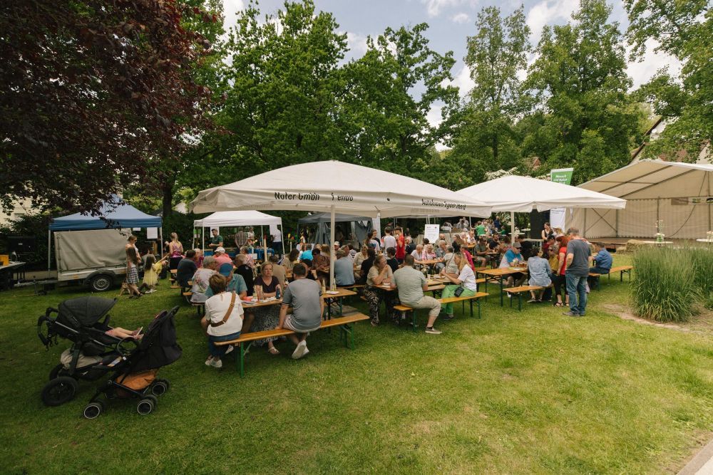Menschen sitzen an Tischen unter Sonnenschirmen