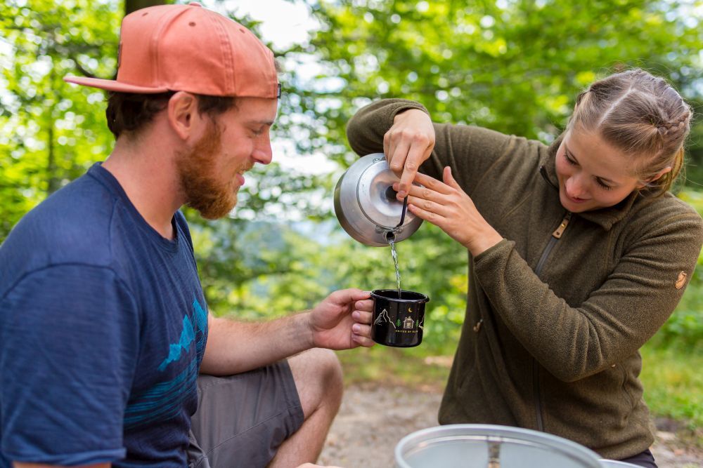 Eine Frau gießt Wasser aus in eine Tasse.