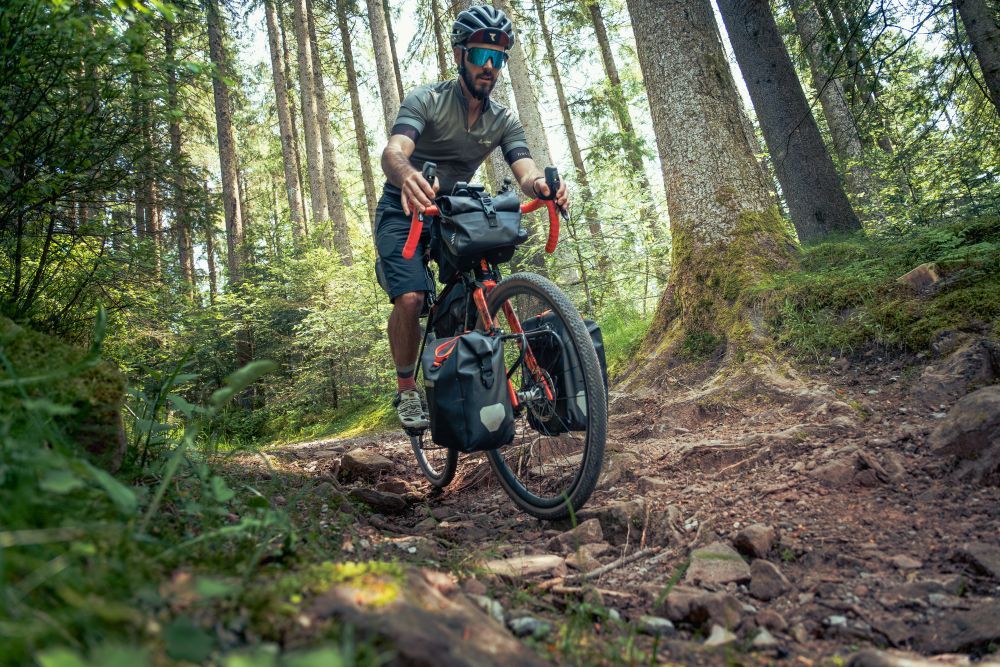 Ein Mann fährt auf einem Gravel Bike einen steinigen Wald-Trail hinunter.