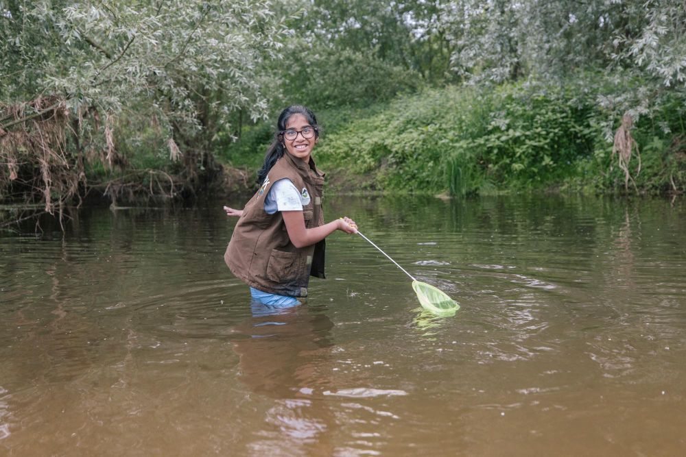 Mädchen steht mit einem Ketscher in einem Fluss.