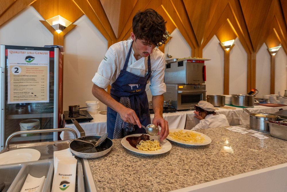 Ein junger Mann richtet einen Teller mit Spätzle und einem Stück Fleisch mit Soße.
