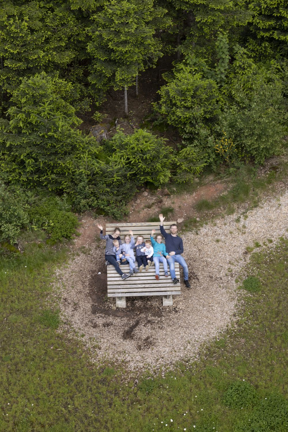 Eine Familie liegt auf einer hölzernen Sonnenliege am Waldrand.