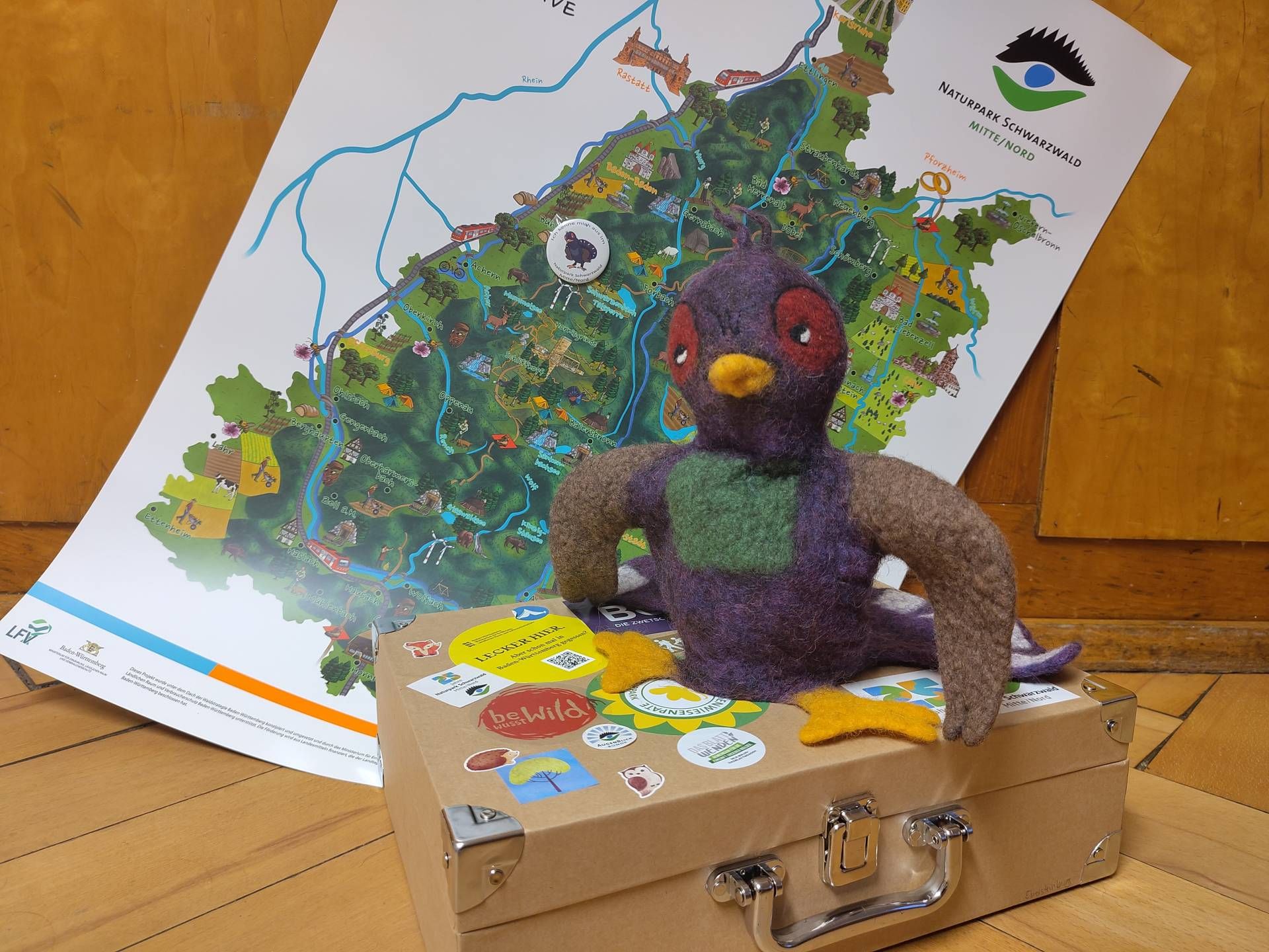Filzpuppe Urli sitzt auf einem Koffer vor der Naturpark-Karte.
