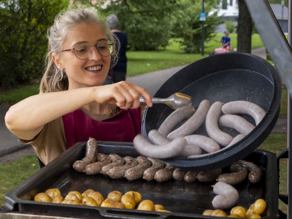 Junge Frau legt Würste auf einen Grill.