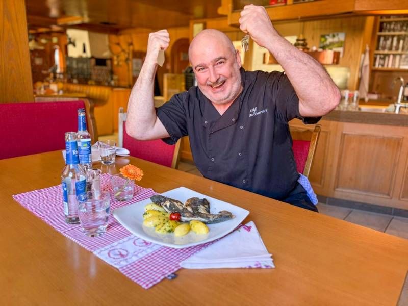 Küchenchef Ralf Finkbeiner hält Gabel und Fischmesser in den Händen, sitzt am gedeckten Tisch mit seiner frisch zubereiteten Schwarzwaldforelle