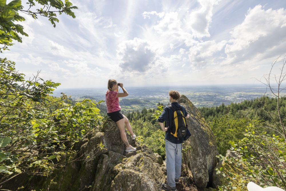 Ein junges Paar steht auf einem Felsen und schaut über die Schwarzwälder Vorbergzone ins Rheintal. Foto: Naturpark Schwarzwald Mitte/Nord e. V.