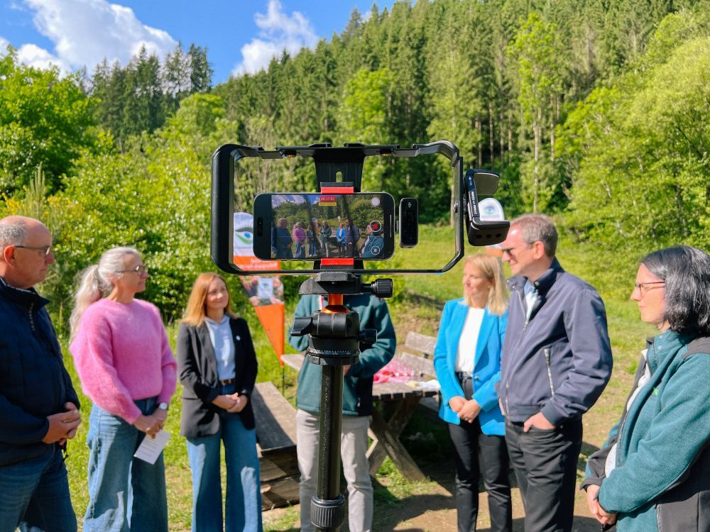 Handy in einer Halterung fotografiert eine Menschengruppe