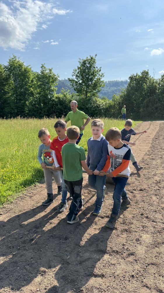 Kinder ziehen Walze über eine eingesäte Fläche.