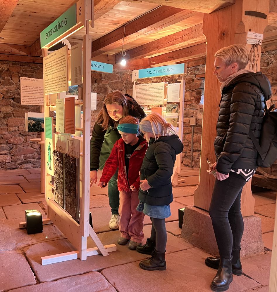 Zwei Frauen und zwei Mädchen stehen vor einer Ausstellungsstellwand