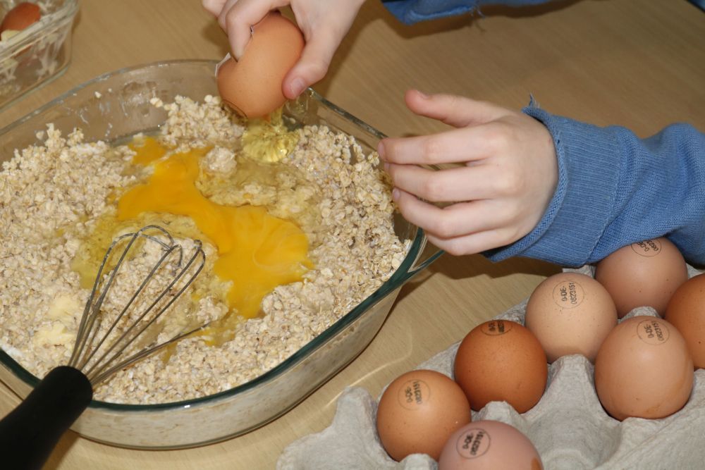 Kind schlägt ein Ei an einer Schüssel auf.